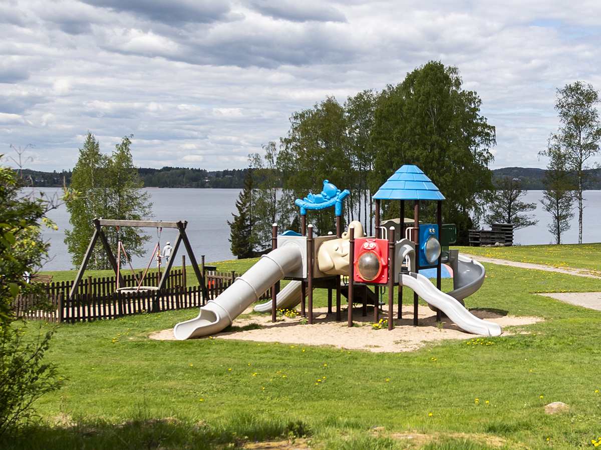 Lekplats med rutschbanor och gunga med utsikt över vattnet.