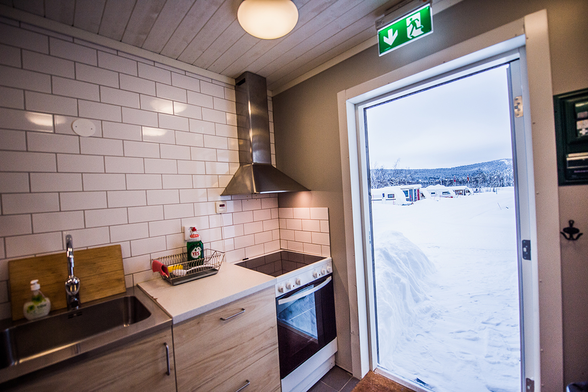 Köksdel i servicebyggnad med utsikt genom glasdörren mot vintermiljö utanför.