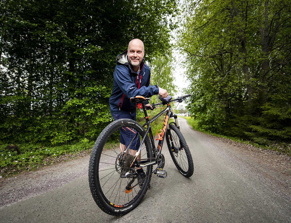 Magnus står lutad mot sin cykel mitt på en grusväg som går genom en grön och lummig skog